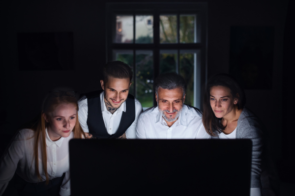 A group of businesspeople with computer indoors in office, working late.