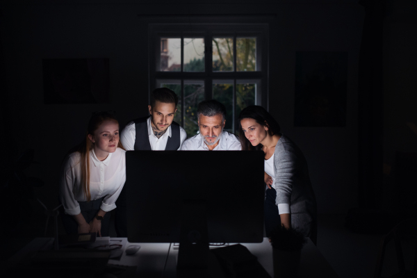 A group of businesspeople with computer indoors in office, working late.