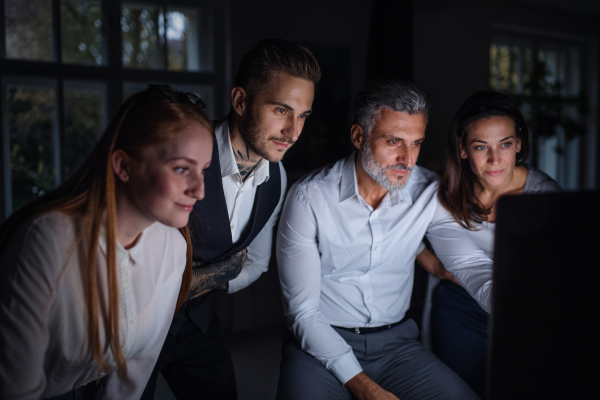 A group of businesspeople with computer indoors in office, working late.