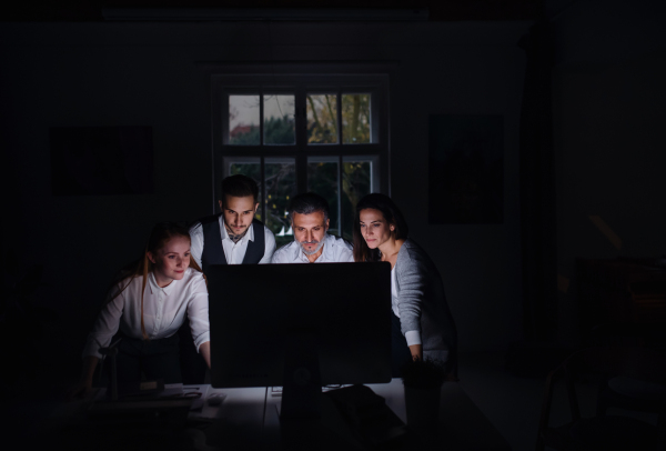 A group of businesspeople with computer indoors in office, working late.