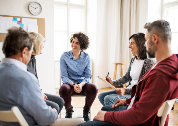 Serious men and women sitting in a circle during group therapy, talking.