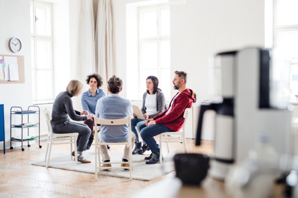 Serious men and women sitting in a circle during group therapy, talking.