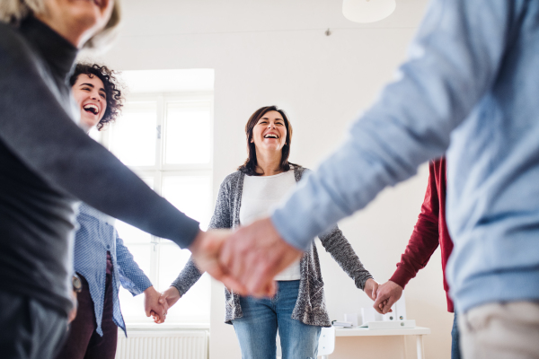 Midsection of people standing in a circle and holding hands during group therapy, laughing.