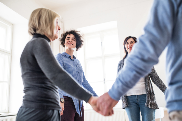 People standing in a circle and holding hands during group therapy, laughing.