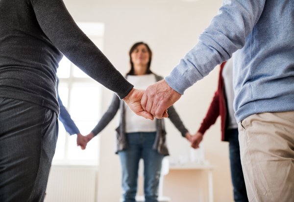 A midsection of people standing in a circle and holding hands during group therapy.