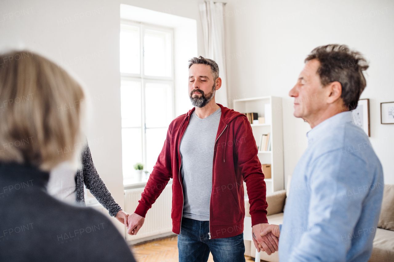 People with closed eyes standing in a circle and holding hands during group a therapy.