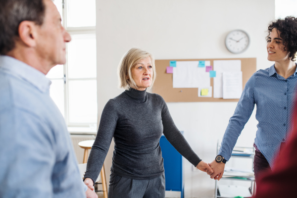 Midsection of people standing in a circle and holding hands during group therapy, talking.