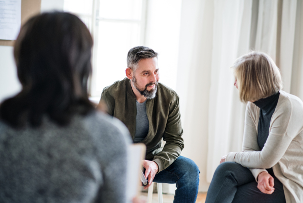 Mature man and senior women sitting in a circle during group therapy, talking.