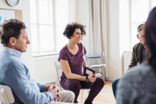 Serious men and women sitting in a circle during group therapy, talking.