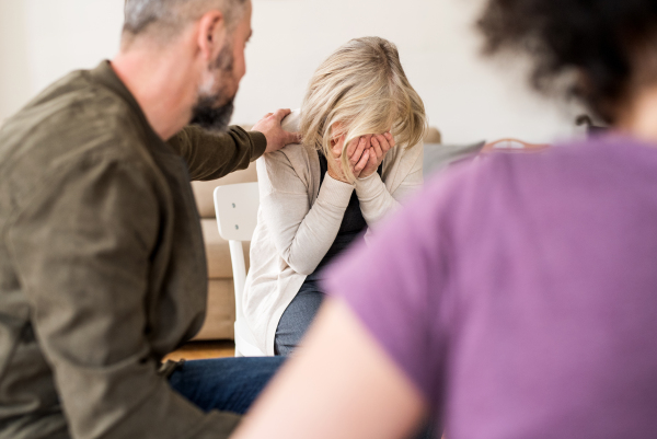 A senior depressed woman crying during group therapy, other people comforting her.