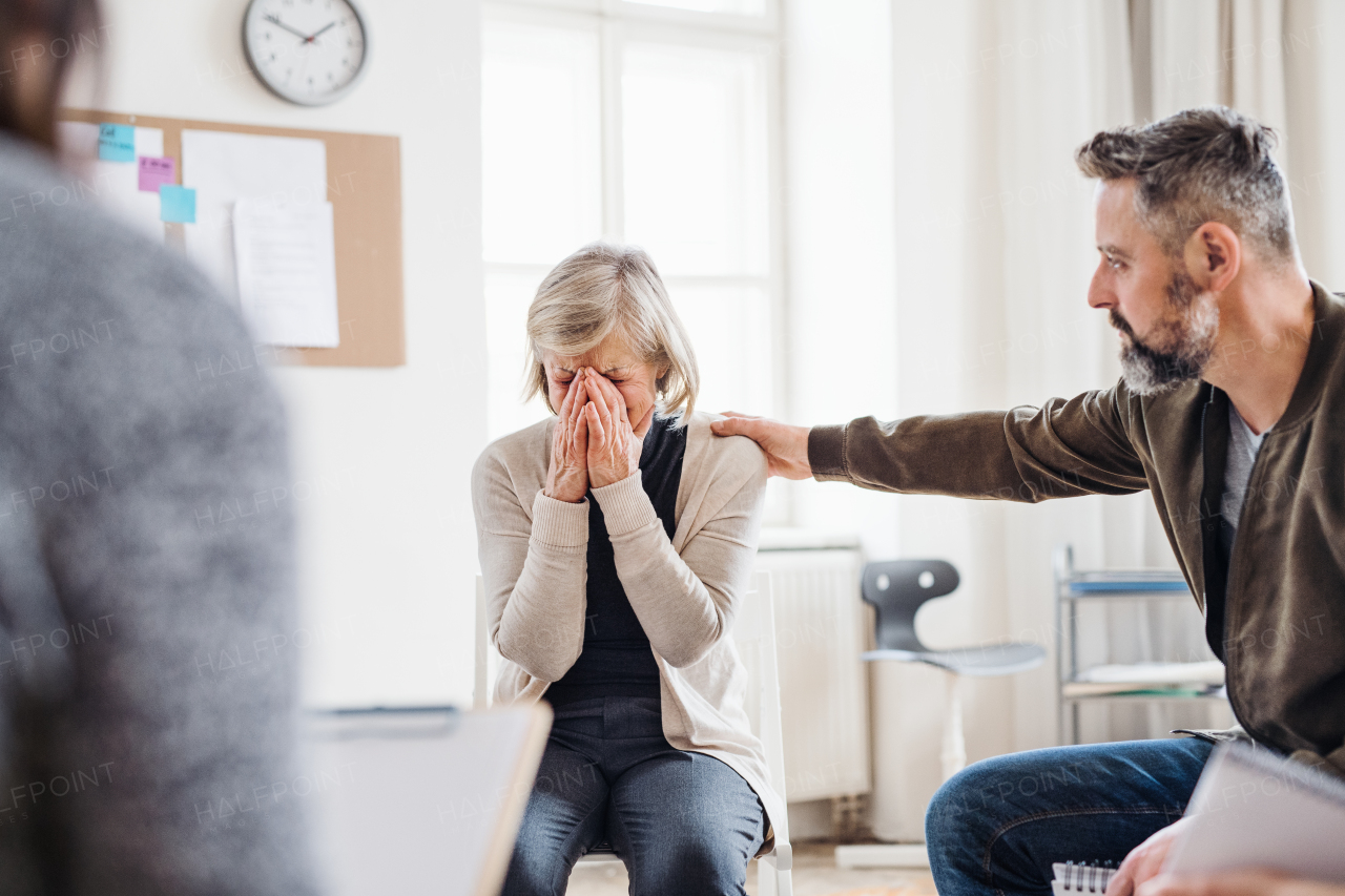 A senior depressed woman crying during group therapy, other people comforting her.