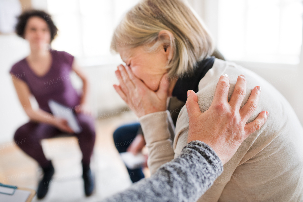 A senior depressed woman crying during group therapy, other people comforting her.