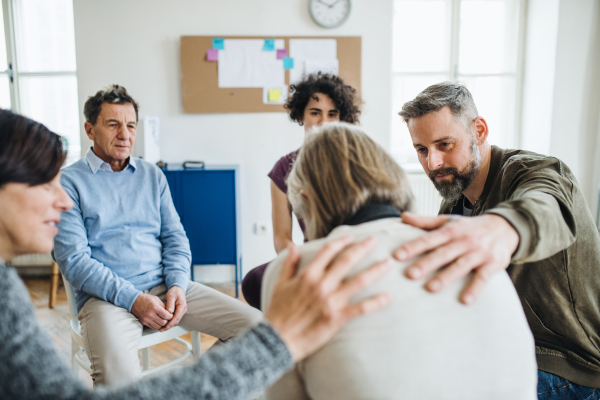 Serious men and women sitting in a circle during group therapy, supporting each other.