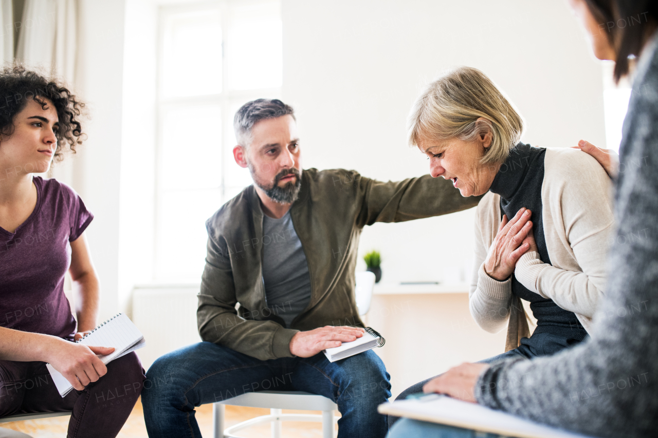 Serious men and women sitting in a circle during group therapy, supporting each other.