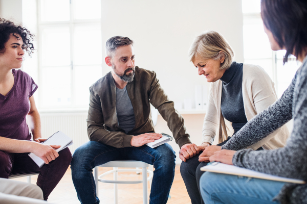 Serious men and women sitting in a circle during group therapy, supporting each other.