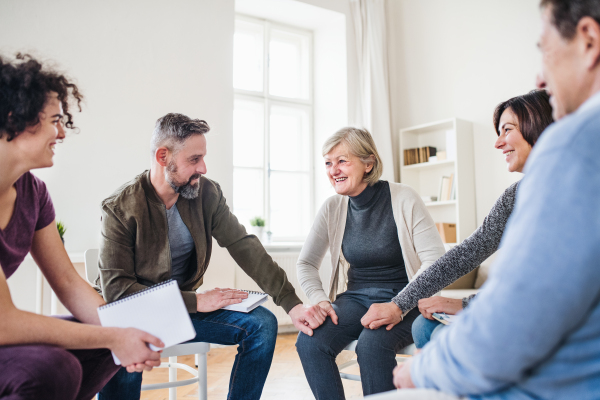 Men and women sitting in a circle and holding hands during group therapy, laughing.