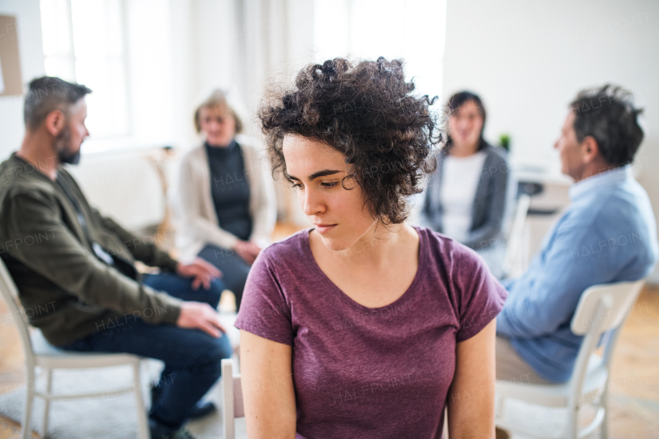 A portrait of young attractive depressed woman during group therapy.