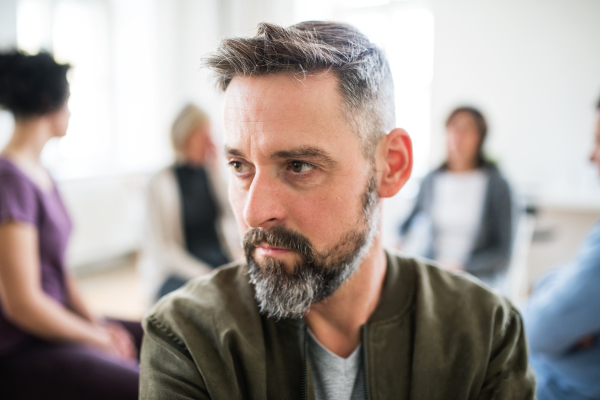 A waist-up portrait of senior depressed man during group therapy.