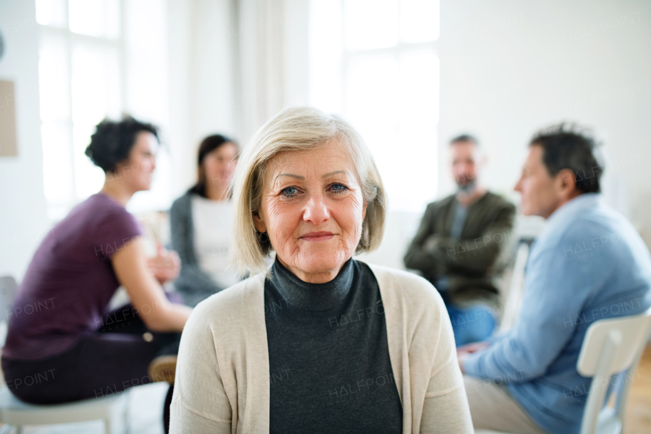 A waist-up portrait of senior depressed woman during group therapy.