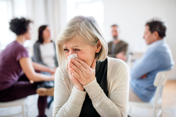 A portrait of senior depressed woman crying during group therapy, wiping her tears.