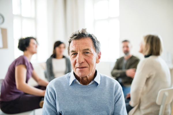 A waist-up portrait of senior depressed man during group therapy.