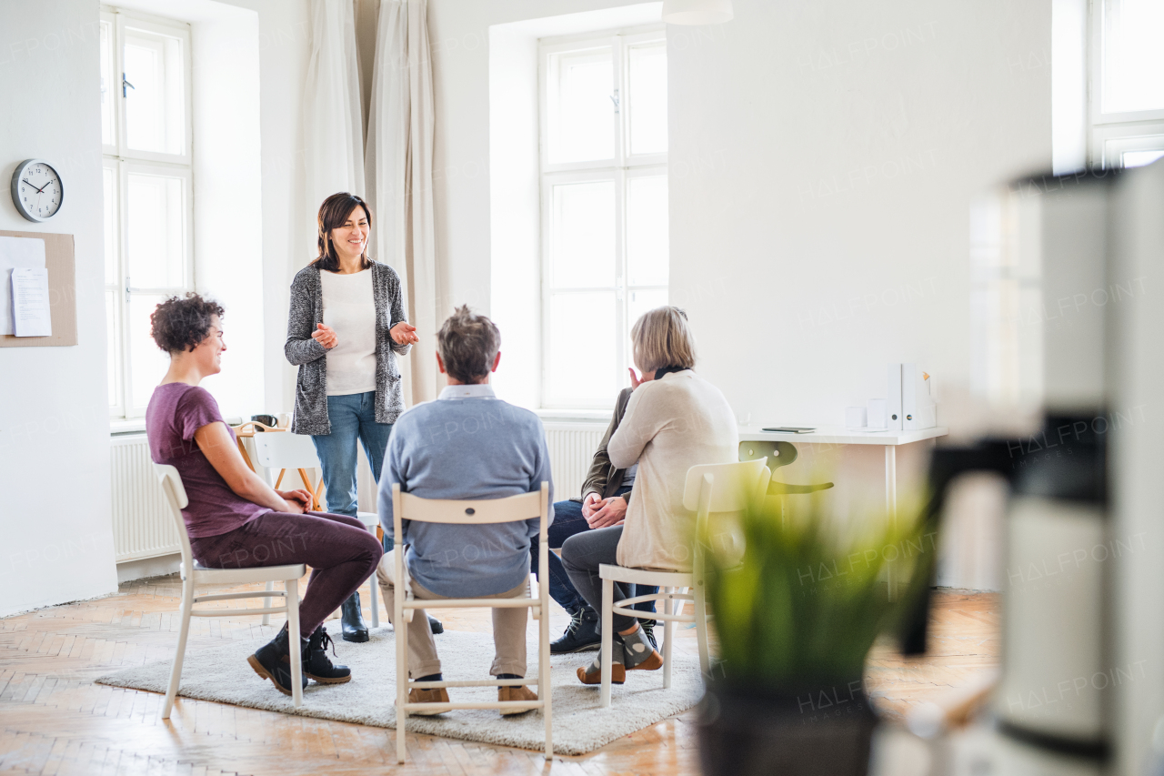 A senior woman standing and talking to other people during group therapy.