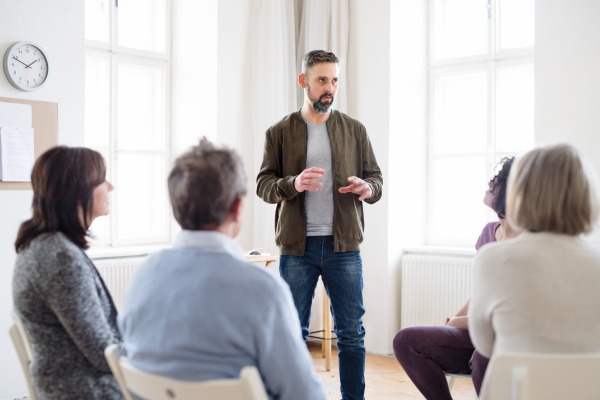 A mature man standing and talking to other people during group therapy.