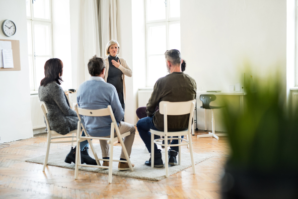 A senior woman standing and talking to other people during group therapy.