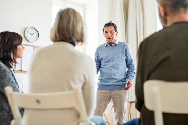 A mature man standing and talking to other people during group therapy.