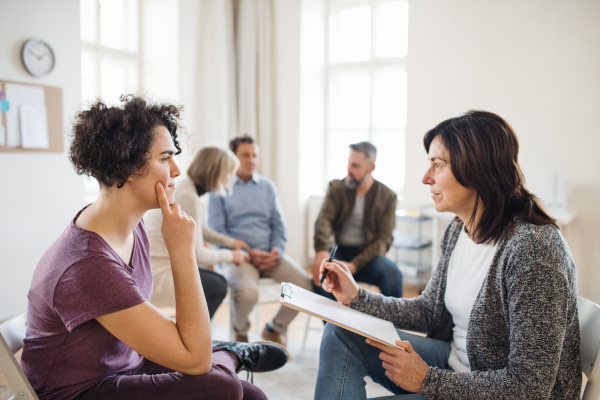 A senior counselor with clipboard talking to a young woman during group therapy.