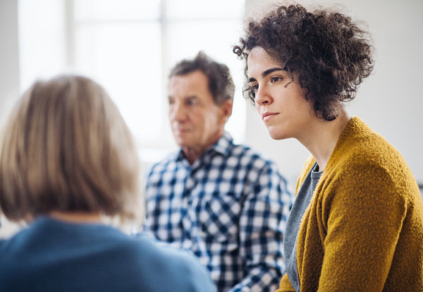 Serious men and women sitting in a circle during group therapy, talking.