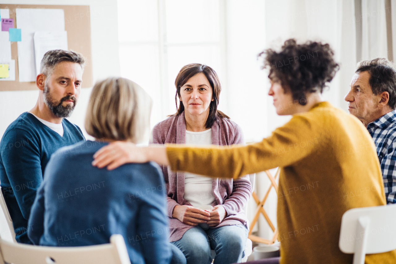 Serious men and women sitting in a circle during group therapy, supporting each other.