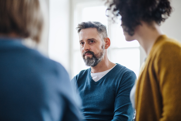 Midsection of serious men and women sitting in a circle during group therapy, talking.