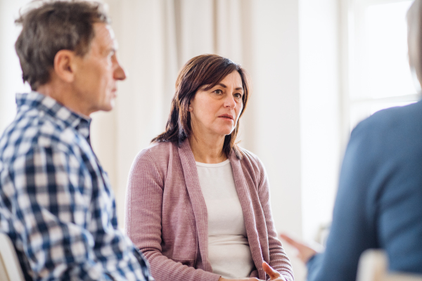 Serious men and women sitting in a circle during group therapy, talking.