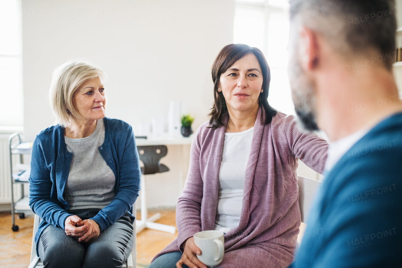 Serious men and women sitting in a circle during group therapy, supporting each other.