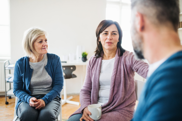 Serious men and women sitting in a circle during group therapy, supporting each other.