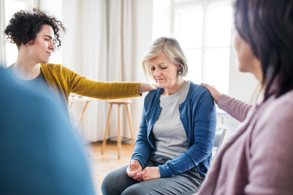 Serious men and women sitting in a circle during group therapy, supporting each other.