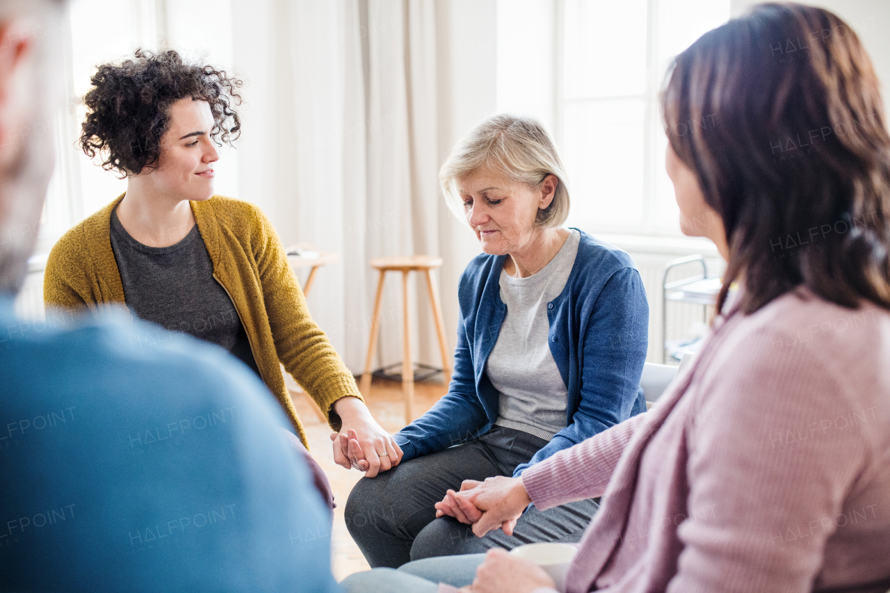 Serious men and women sitting in a circle during group therapy, supporting each other.