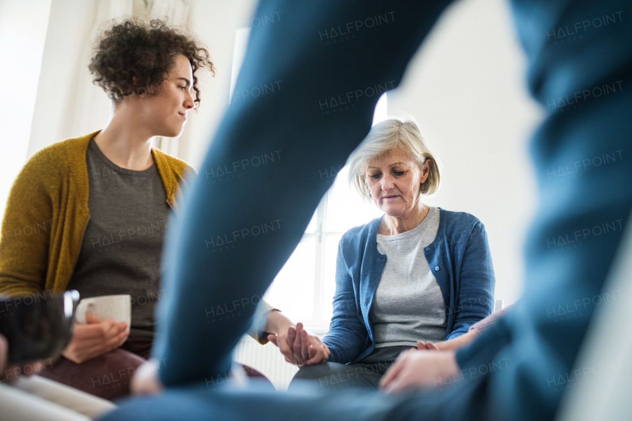 Serious men and women sitting in a circle during group therapy, supporting each other.