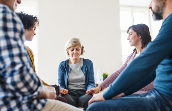 Men and women sitting in a circle and holding hands during group therapy, eyes closed.