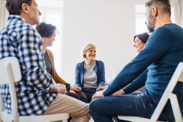 Men and women sitting in a circle and holding hands during group therapy, laughing.