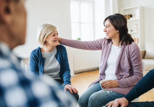 Serious men and women sitting in a circle during group therapy, supporting each other.