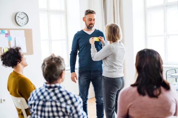 A counsellor putting an adhesive note with the word sad on client during group therapy.