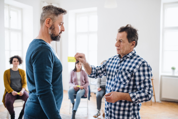 A counsellor putting an adhesive note with the word angry on client during group therapy.