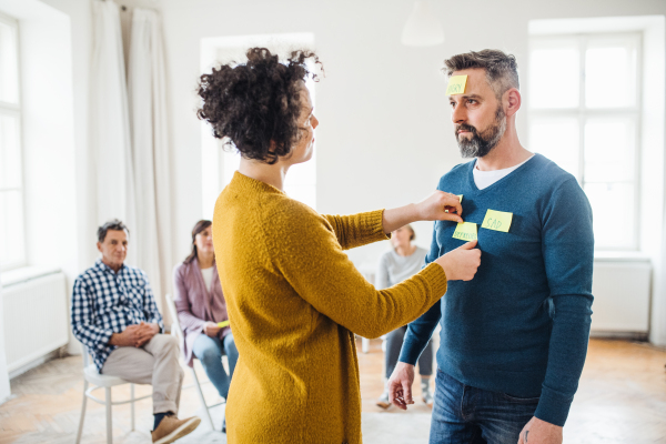 A counsellor putting adhesive notes with the word sad on client during group therapy.