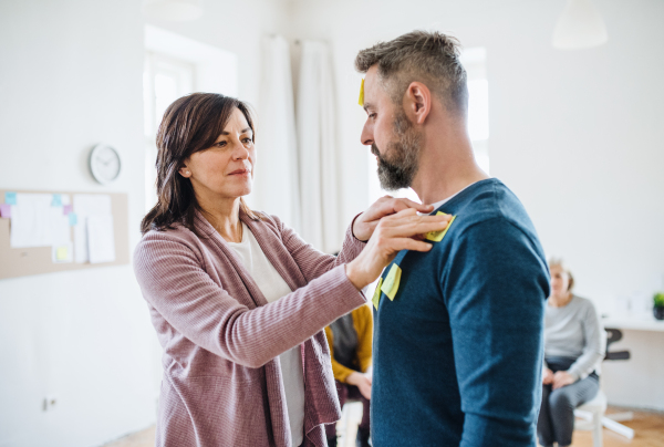 A counsellor putting an adhesive note with negative emotions words on client during group therapy.