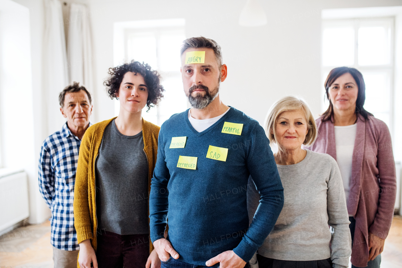 A portrait of young and old people standing with negative emotions adhesive notes during group therapy.