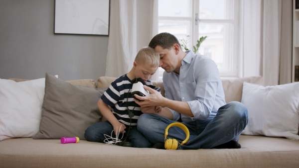 A father with happy down syndrome son indoors at home, using vr goggles.