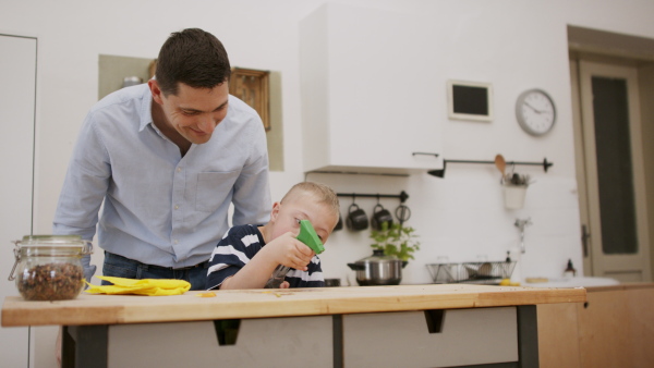 A father with happy down syndrome son indoors in kitchen, cleaning table.