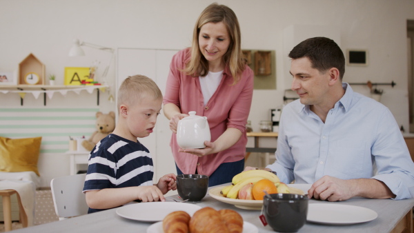 A happy family with down syndrome son at the table, having breakfast.